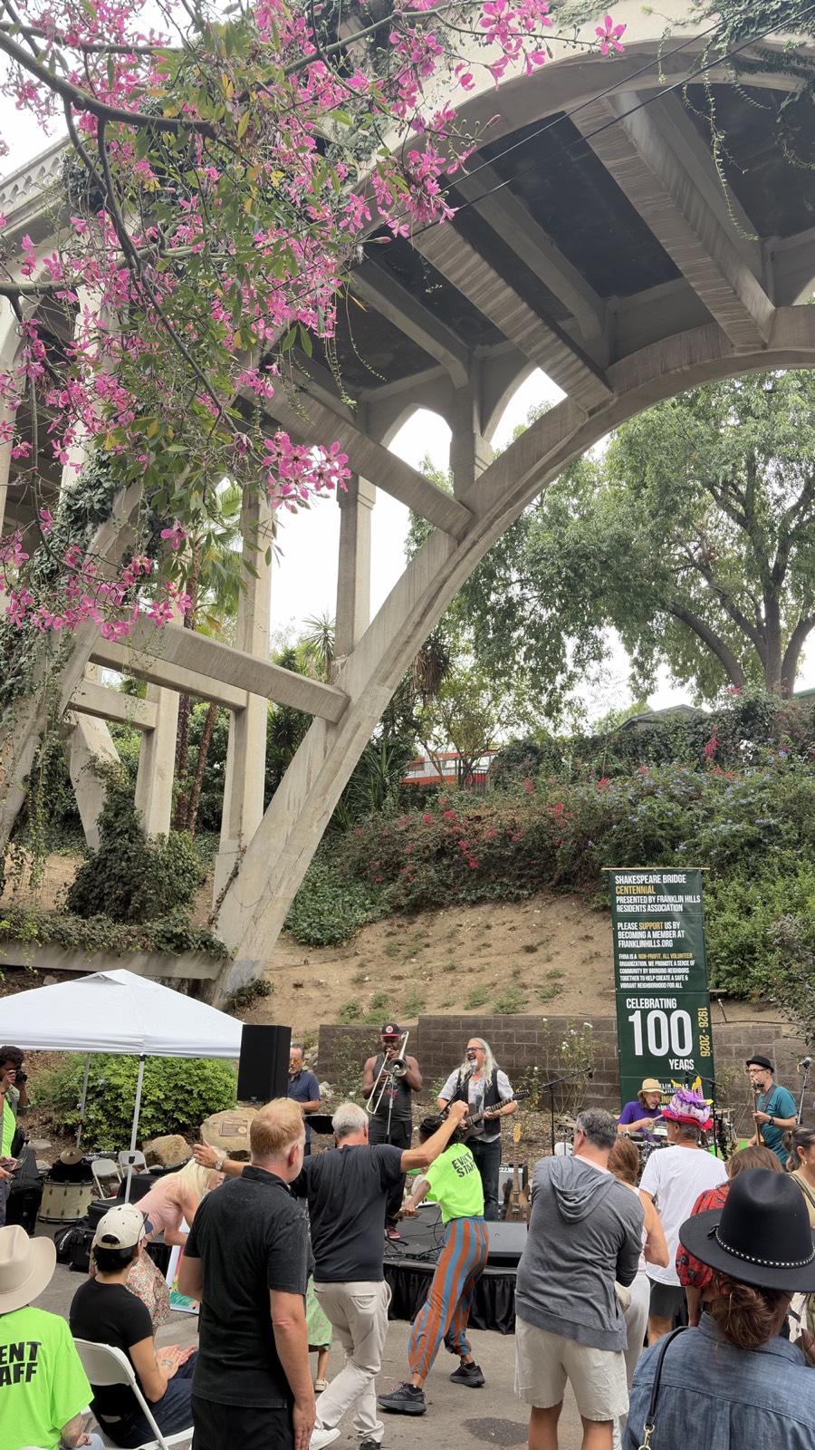 A band playing beneath the arch of the Shakespeare Bridge beside a banner reading Celebrating 100 Years